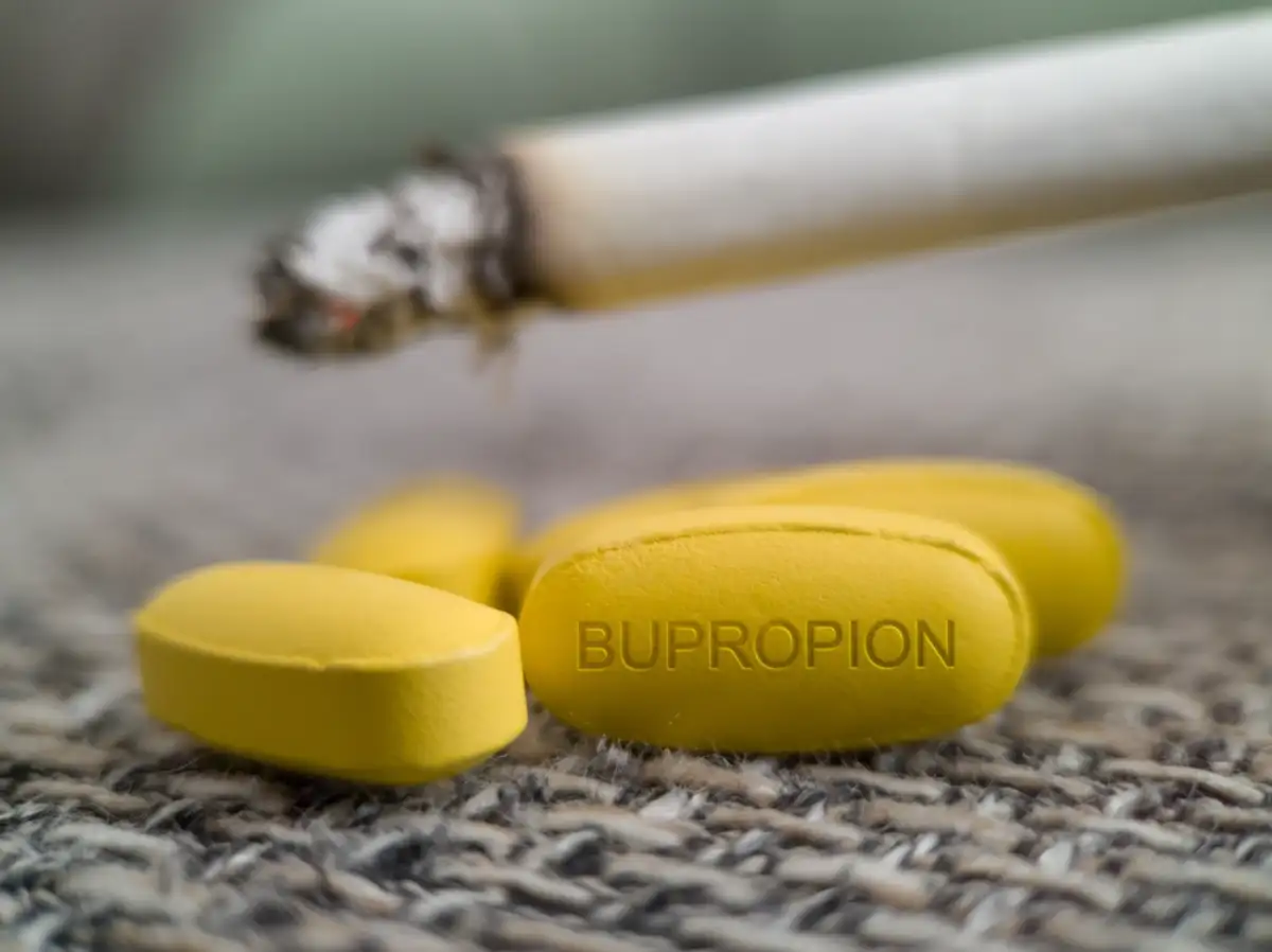 Bupropion yellow pill with cigarette in background