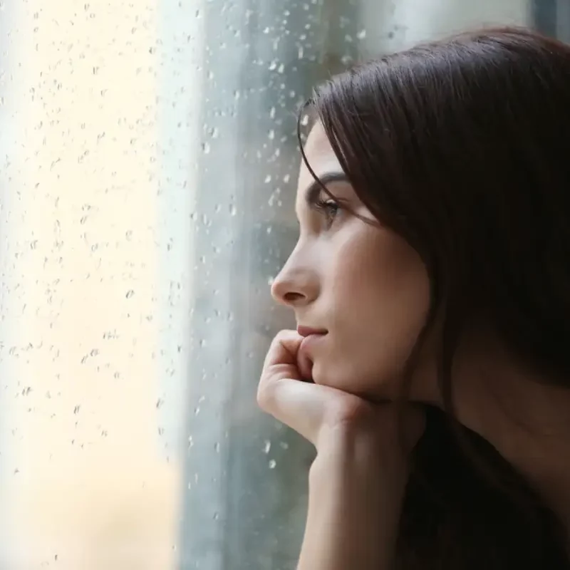 Depressed young woman near window at home