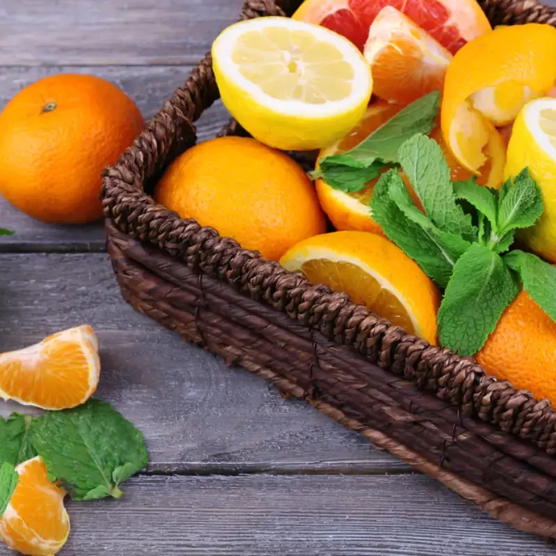 Fresh citrus fruits with green leaves in wicker basket on wooden background