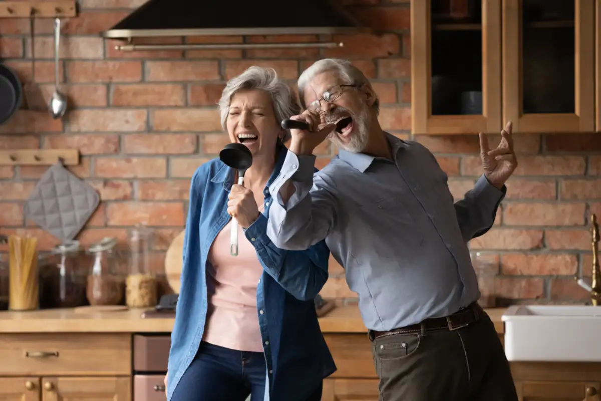 Happy senior husband and wife have fun sing in kitchen appliances cooking together at home