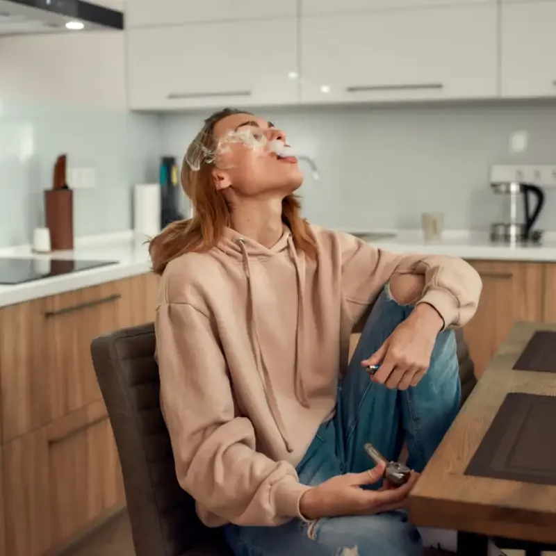 Young woman exhaling the smoke while smoking marijuana from a metal pipe