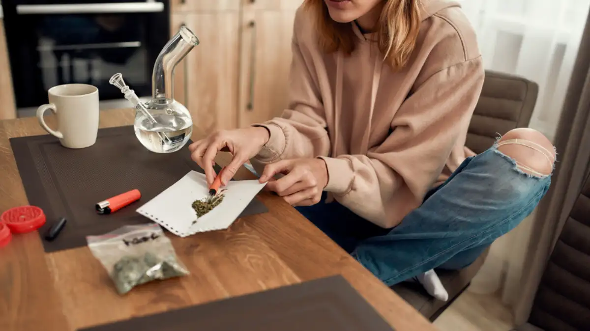 Young woman putting weed in a tube while sitting in the kitchen