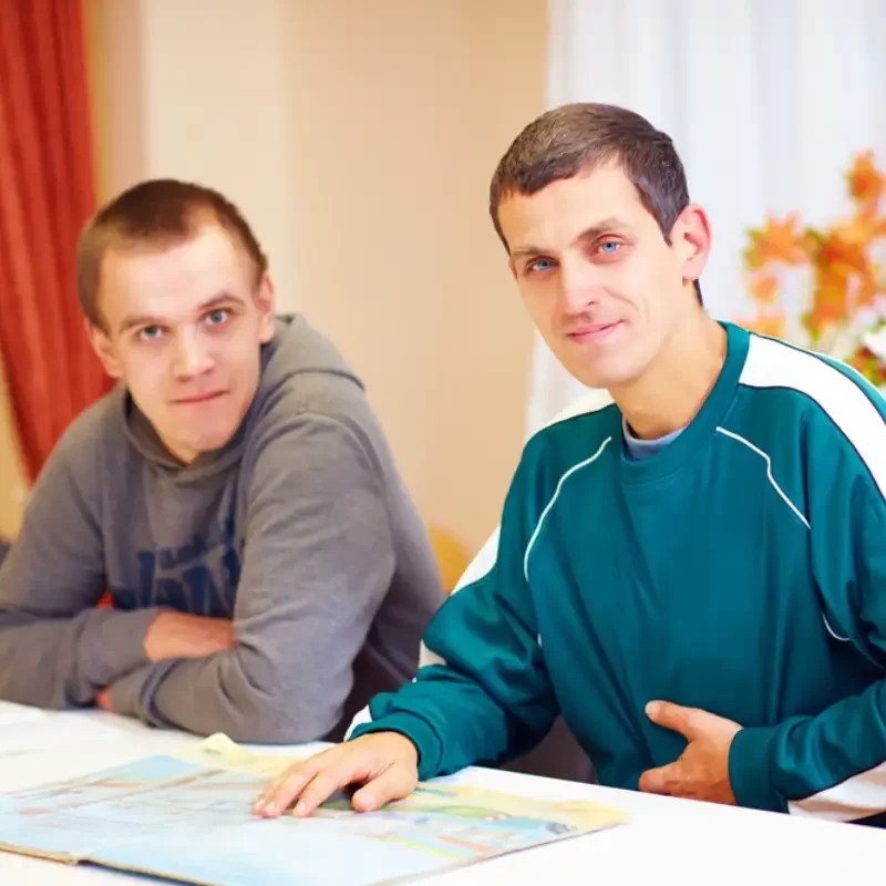 cheerful adult men with disability sitting at the desk in rehabilitation center