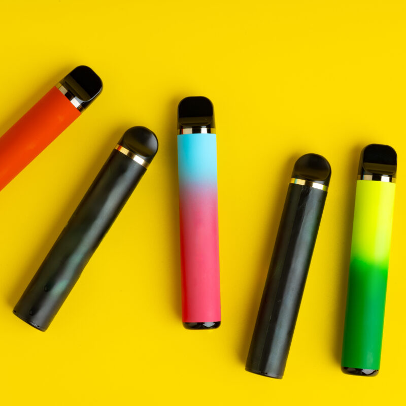 Colorful disposable electronic cigarettes on yellow background